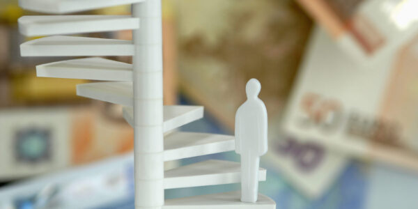 Figur auf Treppe mit Geldscheinen im Hintergrund (Symbolbild) © Westend61 / Achim Sass