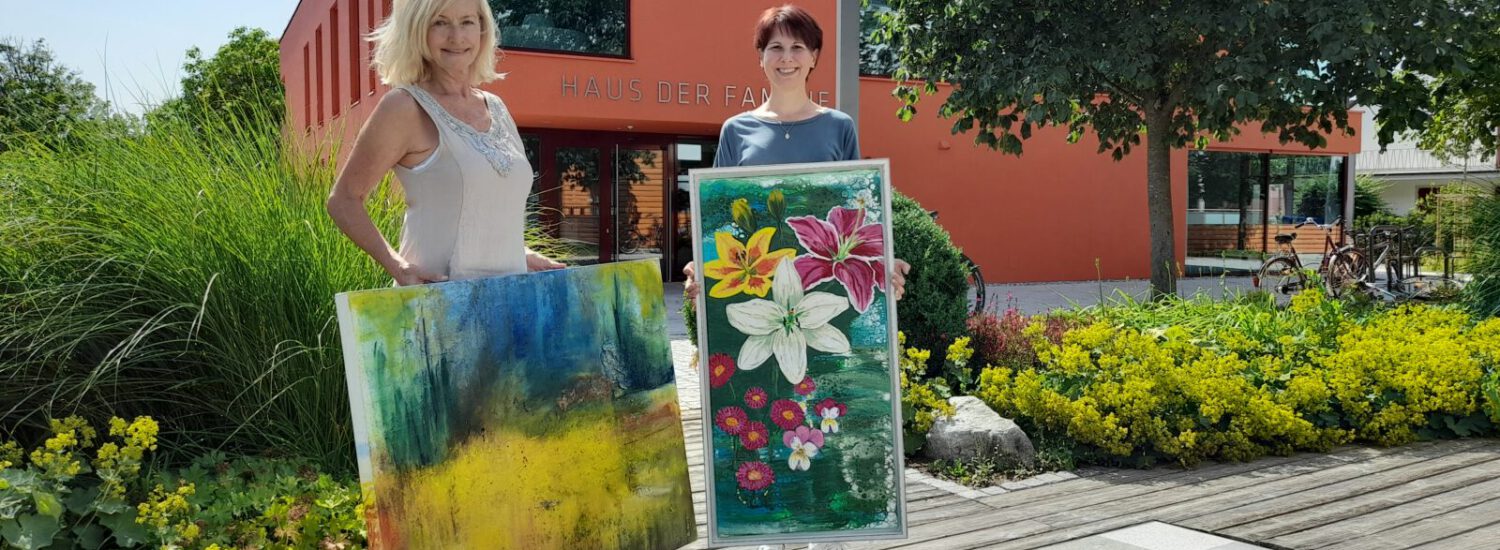 Zwei Frauen präsentieren zwei Gemälde vorm Haus der Familie © Stadt Burghausen