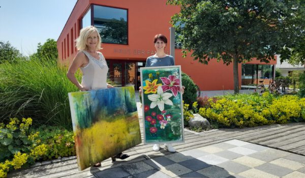 Zwei Frauen präsentieren zwei Gemälde vorm Haus der Familie © Stadt Burghausen