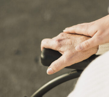 Hand hält Hand einer älteren Person im Rollstuhl © Westend61 / Uwe Umstätter
