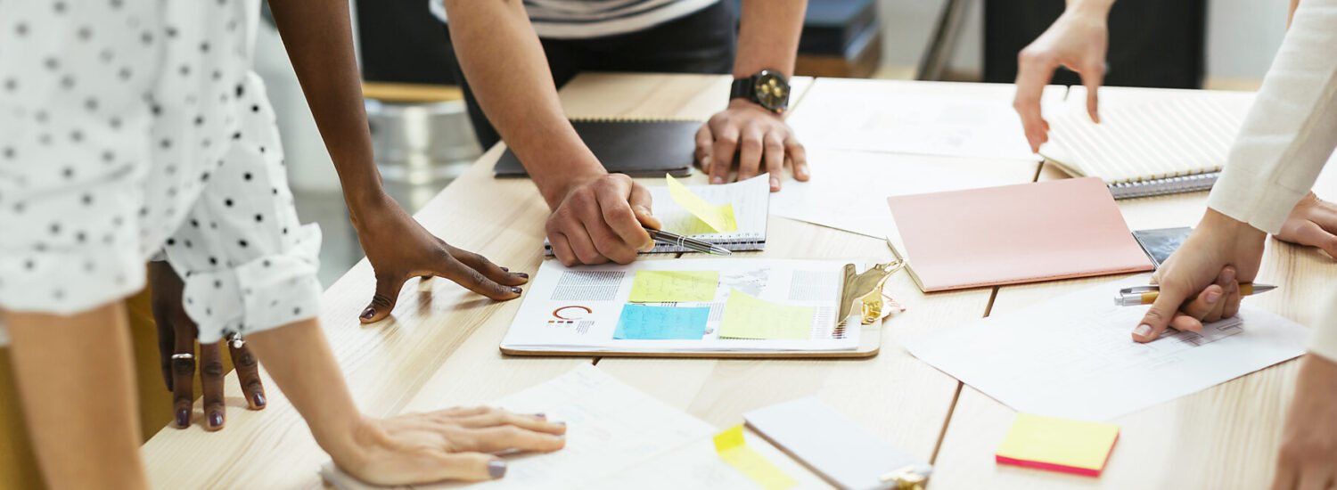 Nahaufnahme von Personen, die über einem Tisch mit Unterlagen gebeugt sind © Westend61 / Bonninstudio