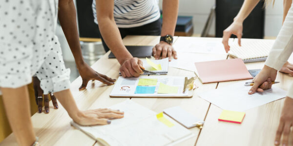 Nahaufnahme von Personen, die über einem Tisch mit Unterlagen gebeugt sind © Westend61 / Bonninstudio