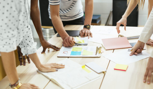 Nahaufnahme von Personen, die über einem Tisch mit Unterlagen gebeugt sind © Westend61 / Bonninstudio