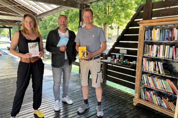 PM 152 Bücherschrank am Wöhrsee neben Eingang mit Schreiner und Leitung Bauhof sowie Bibliothek Glückliche Gesichter bei den Bücherschrank- und Literatur-Lieferungen am Wöhrsee und im Freibad. Christin Moll, Leiterin der Stadtbibliothek, Peter Schweikl, Leiter Bauhof, Markus Salzinger Schreiner im Bauhof und Florian Moser von der Bäderleitung der Bäder Burghausen. Fotocredit: Stadt Burghausen / Königseder