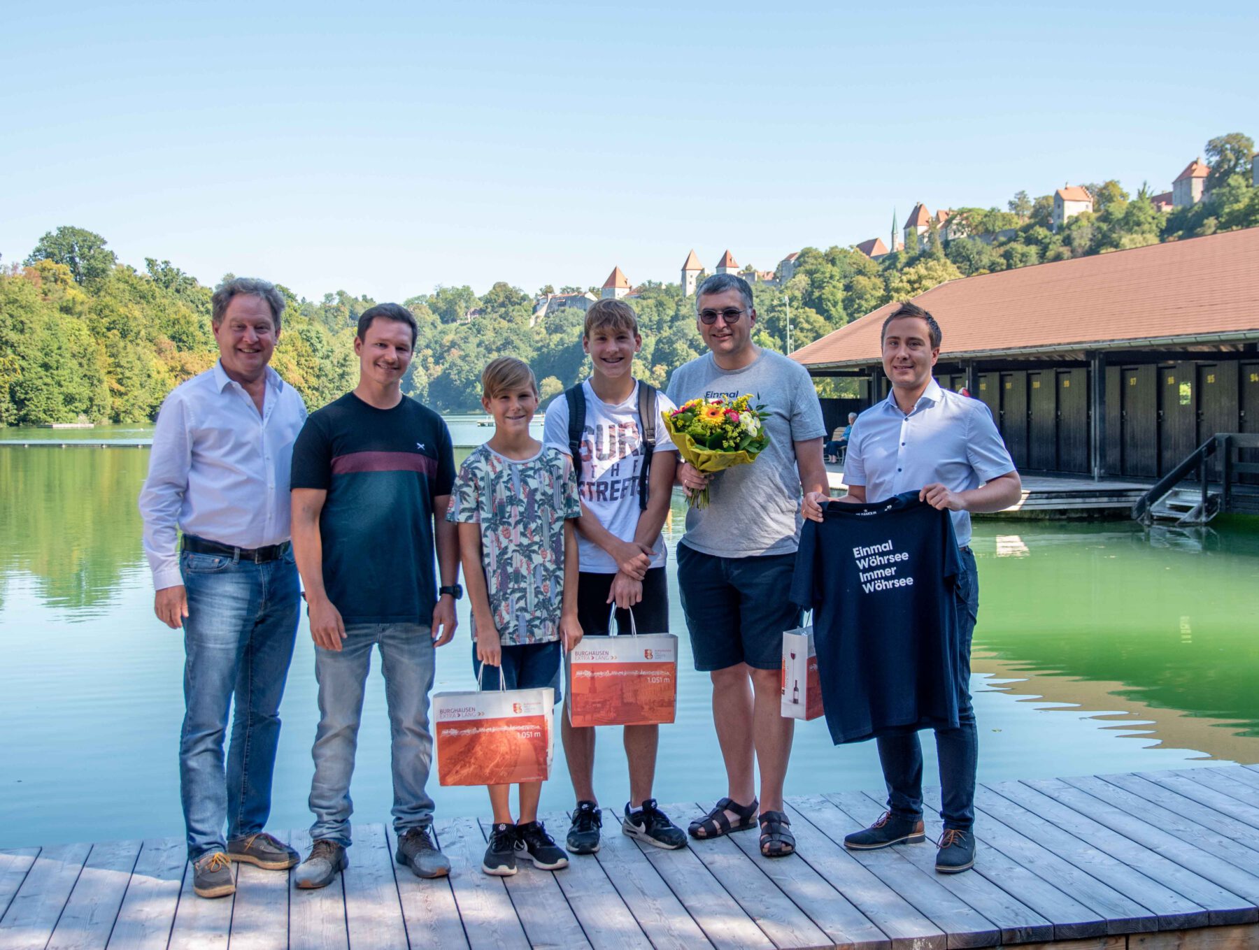 Familie Waas bekam ein Geschenk, denn Sohn Jakob war der 100.000ste Badegast. Im Geschenk waren z.B. Flip Flops, Schwimmbrillen und ein Wöhrsee-Tshirt sowie eine Saisonkarte für 2024. V.l.n.r.: Erster Bürgermeister Florian Schneider, Wöhrseebad-Betriebsleiter Dennis Clemens, Jakob und Felix Waas, Bernhard Waas und kaufmännischer Bäderleiter der Bäder Burghausen Stefan Sajdak © Stadt Burghausen/ebh