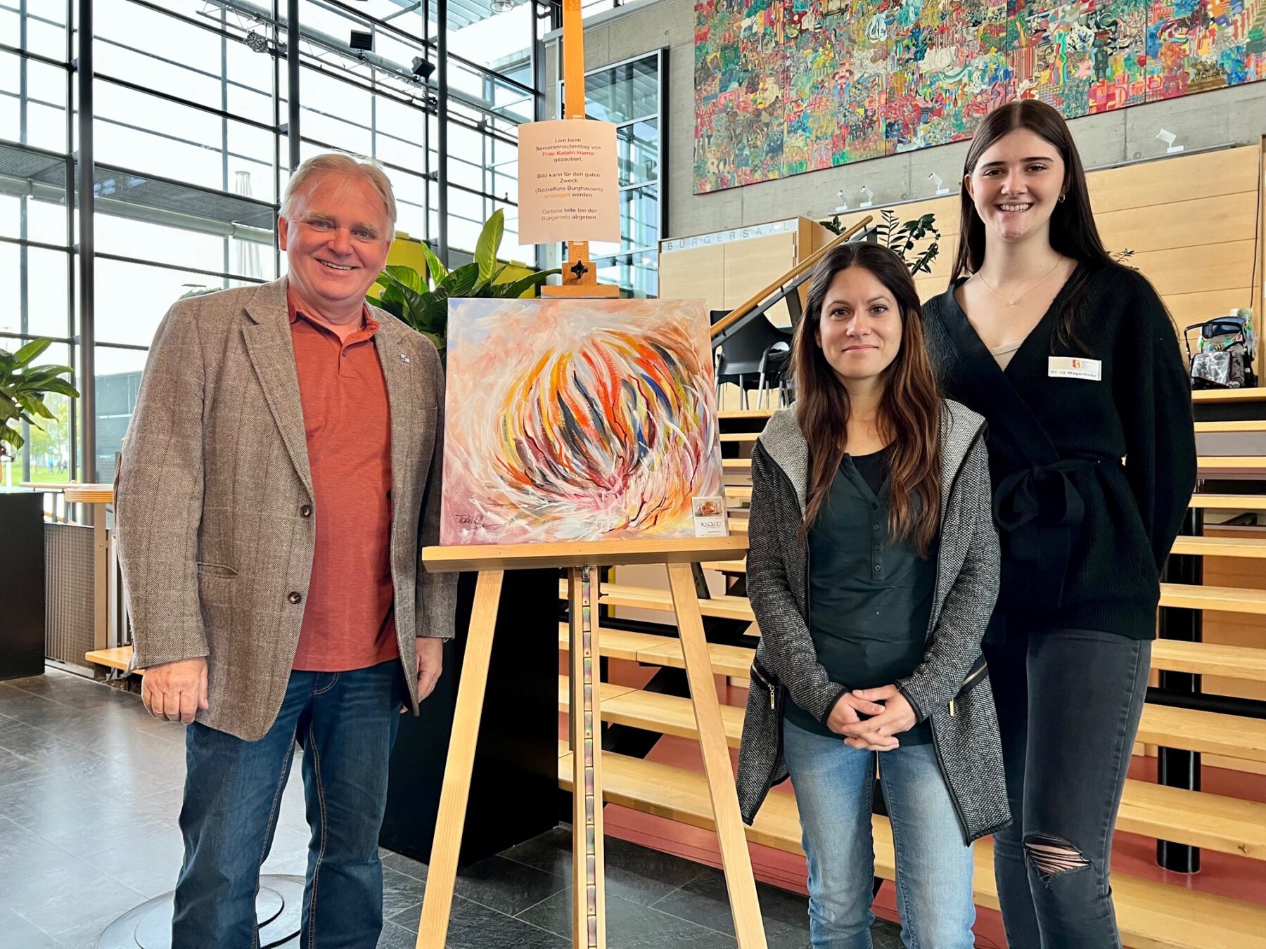 Foto –„Live-Arbeit“ beim Seniorennachmittag: Die Burghauser Künstlerin Katalin Harrer zauberte ein ausdrucksstarkes Motiv auf die Leinwand, das für einen guten Zweck meistbietende versteigert werden soll. Seniorenreferent Heiz Donner, Katrin Scheitz (v.l.) und Elena Wagenhofer freuen sich auf hoffentlich viele Gebote. Fotocredit: Stadt Burghausen /köx