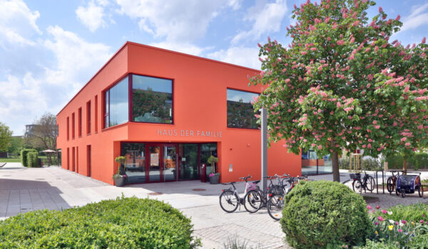 Aussenansicht vom Haus der Familie am Bürgerplatz: Ein Haus mit einer roten Fassade, Fahrräder und Bäume im Vordergrund