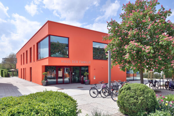 Aussenansicht vom Haus der Familie am Bürgerplatz: Ein Haus mit einer roten Fassade, Fahrräder und Bäume im Vordergrund