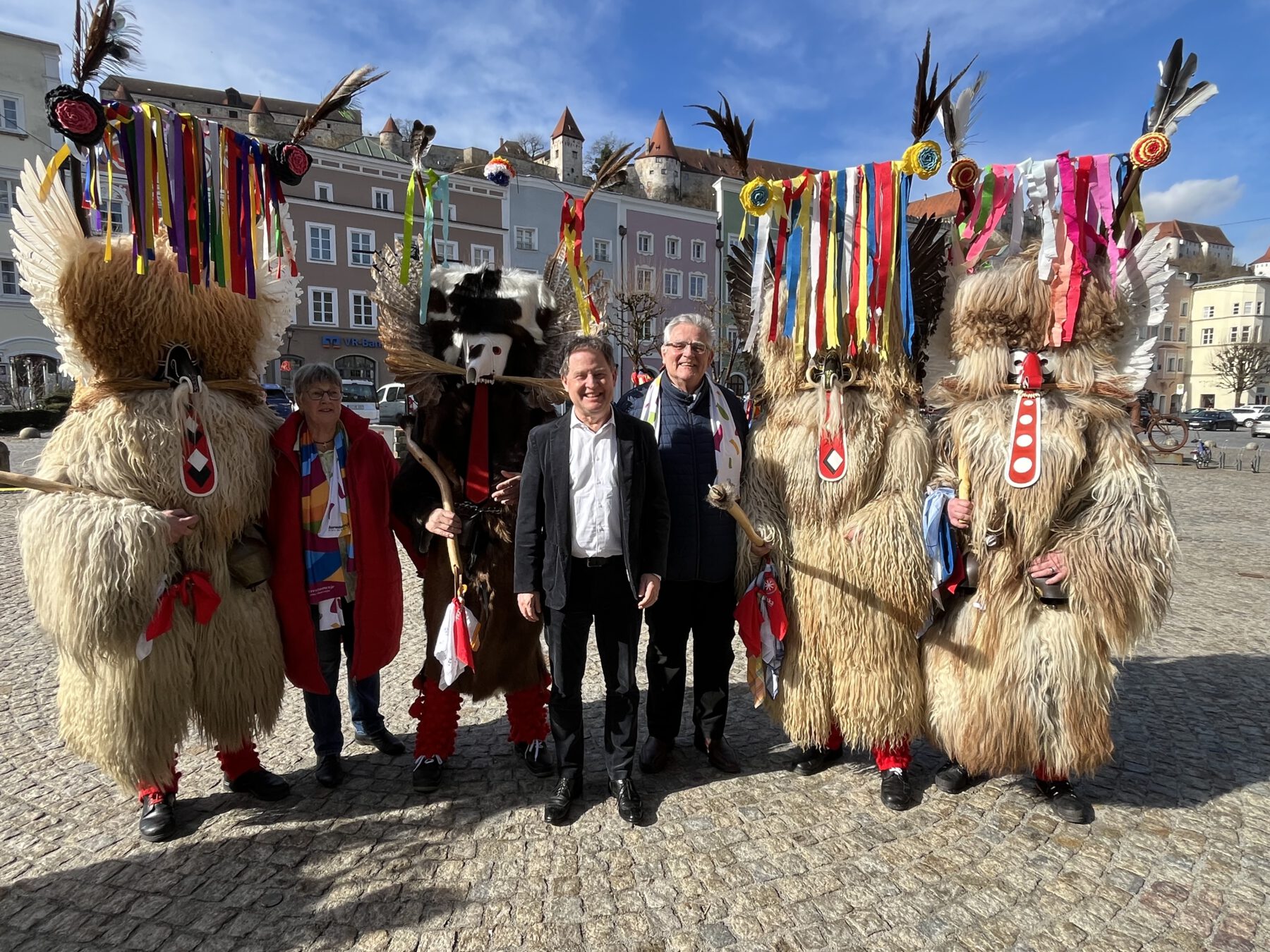 Foto: Im Kreise wilder Kerle: Elisabeth Hübner (2 v.l.), Referentin des Burghauser Partnerstadtvereins für Ptuj, Erster Bürgermeister Florian Schneider und Zweiter Bürgermeister Norbert Stranzinger (Mitte), umringt von einigen Ptujer Kurenten mit ihren farbenprächtigen Masken und mächtigen Knüppeln. Fotocredit: Stadt Burghausen/sast