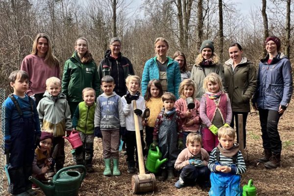 Die Kinder des Montessori Waldkindergarten Burghausen mit FÖJlerin Annalena Wallner (nicht im Bild Joel Feige), den Betreuerinnen und Erzieherinnen vom Waldkindergarten, der Naturschutzbeauftragten Susanne Unterstaller und Ines Huber vom städtischen Umweltamt. Vorne links ist eine frisch gepflanzte Elsbeere zu sehen, die die Kinder auch sofort noch gegossen haben. Fotocredit: Stadt Burghausen / köx