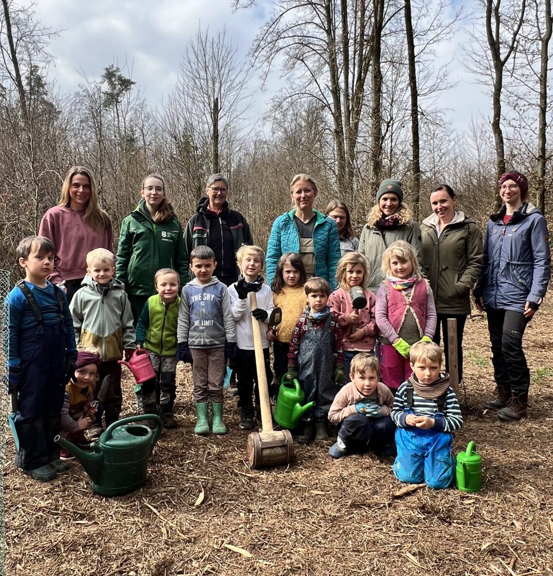 Die Kinder des Montessori Waldkindergarten Burghausen mit FÖJlerin Annalena Wallner (nicht im Bild Joel Feige), den Betreuerinnen und Erzieherinnen vom Waldkindergarten, der Naturschutzbeauftragten Susanne Unterstaller und Ines Huber vom städtischen Umweltamt. Vorne links ist eine frisch gepflanzte Elsbeere zu sehen, die die Kinder auch sofort noch gegossen haben. Fotocredit: Stadt Burghausen / köx