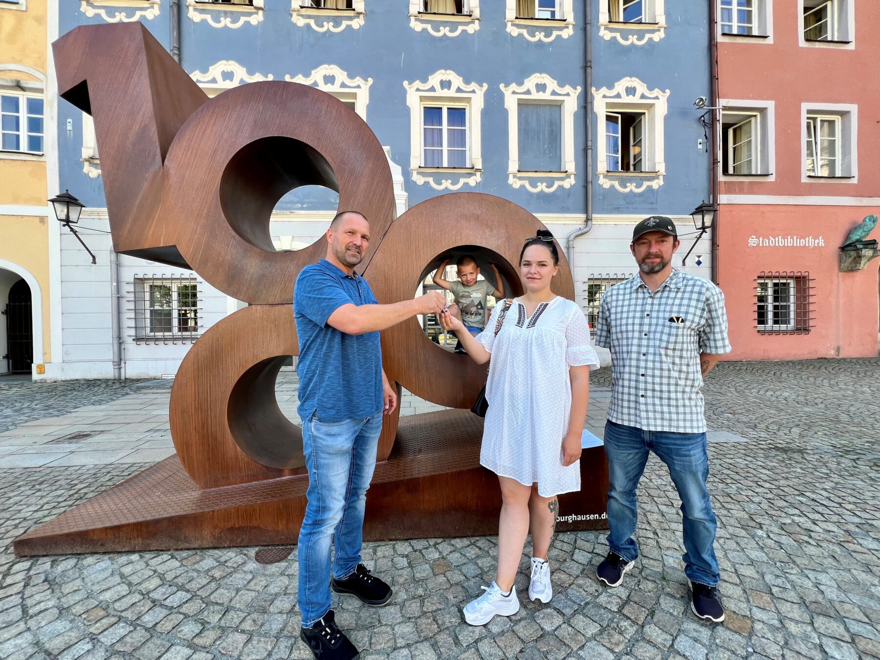 Erfolg durch gute Zusammenarbeit: Wohnungsschlüssel-Übergabe an WOHIN-Projektteilnehmerin Olena Nechvolod (mit Sohn Matvii) durch Herrn Michael Madl (l.), Gebäudemanager der Stadt Burghausen, mit Markus Huber, BRK-Projektleiter (r.). Fotocredit: Stadt Burghausen / köx