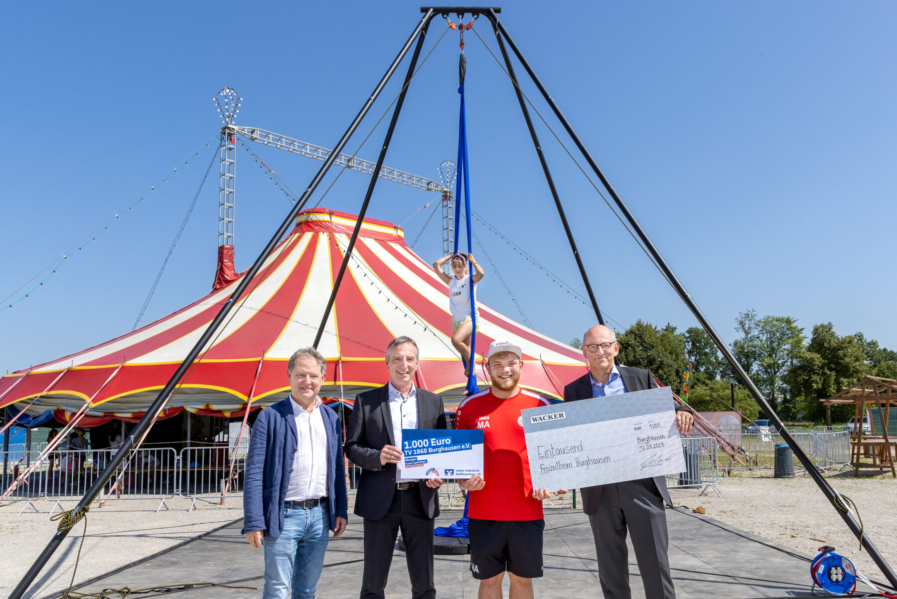 Bei der Spendenscheckübergabe (v. l.): 1. Bürgermeister Florian Schneider, Marktdirektor der VR-Bank im Bereich Burghausen Robert Oberreiter, Leiter Freizeitheim und der Abteilung Zirkus beim TV 1868 Marcel Anslinger sowie WACKER-Werkleiter Peter von Zumbusch. Im Hintergrund Carolina Zellbeck im Luftgestell. (Quelle: Wacker Chemie AG)