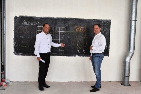 Zeugen der Vergangenheit: Stadtbaumeister Manfred Winkler (l.) und Erster Bürgermeister Florian Schneider begutachten eine Schultafel mit Beschriftung wohl aus den 1960er Jahren, die vor dem Umbau hinter einer Schrankwand versteckt war. Sie wird nun wieder sichtbar in das neue Klassenzimmer integriert. Fotocredit: Stadt Burghausen/tg
