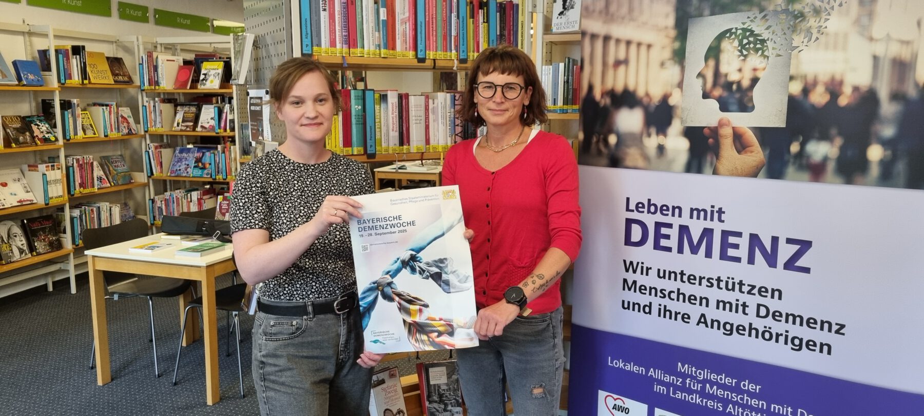 Veronika Alfranseder, Leiterin Seniorenbüro und Quartiersmanagerin der Stadt Burghausen und Christin Moll, Leiterin der Stadtbibliothek Burghausen präsentieren das Plakat zur 6. Bayerischen Demenzwoche, an der sich auch Burghausen mit einem eigenen Programm beteiligt. Fotocredit: Stadt Burghausen / köx