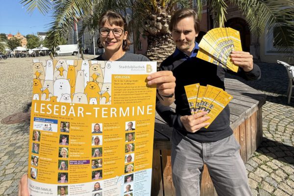 Die Leiterin der Stadtbibliothek Christin Moll und Mitarbeiter Patrick Brenner zeigen das neue Programm „Lesebär aktuell“ 2025 / 2026. Fotocredit: Stadt Burghausen