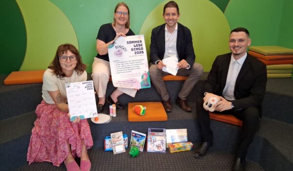 Foto: Vier Stempel einsammeln und – Bingo! So funktioniert der Sommerlesespaß in der Stadtbibliothek. Das Team der Stadtbibliothek mit Leiterin Christin Moll und Mitarbeiterin Monika Vornehm ist bereit für den Kinderansturm, Sebastian Rauschecker und David Gergely-Komaromi von der Sparkasse Burghausen sponserten dieses Mal die Sofortgewinne. Fotocredit: Stadt Burghausen/tg
