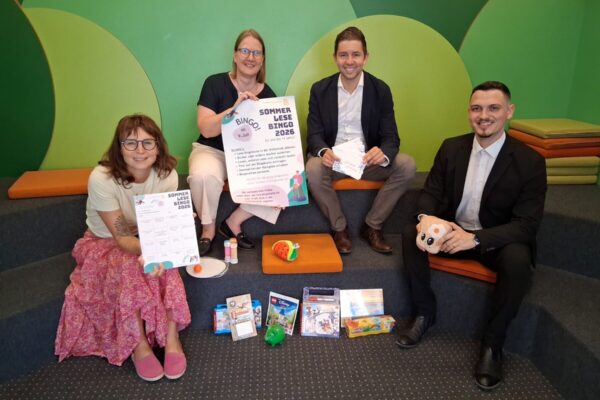 Foto: Vier Stempel einsammeln und – Bingo! So funktioniert der Sommerlesespaß in der Stadtbibliothek. Das Team der Stadtbibliothek mit Leiterin Christin Moll und Mitarbeiterin Monika Vornehm ist bereit für den Kinderansturm, Sebastian Rauschecker und David Gergely-Komaromi von der Sparkasse Burghausen sponserten dieses Mal die Sofortgewinne. Fotocredit: Stadt Burghausen/tg