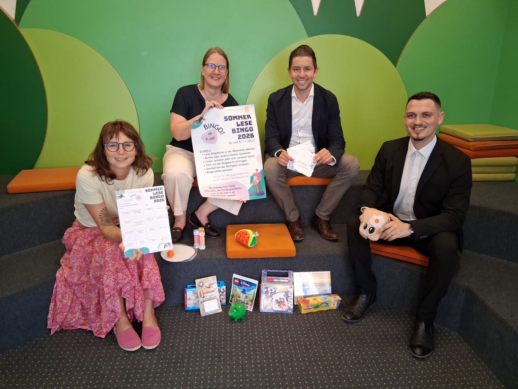 Foto: Vier Stempel einsammeln und – Bingo! So funktioniert der Sommerlesespaß in der Stadtbibliothek  Das Team der Stadtbibliothek mit Leiterin Christin Moll und Mitarbeiterin Monika Vornehm ist bereit für den Kinderansturm, Sebastian Rauschecker und David Gergely Komaromi von der Sparkasse Burghausen sponserten dieses Mal die Sofortgewinne  Fotocredit: Stadt Burghausen/tg