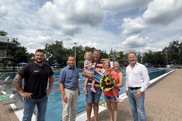 Erster Bürgermeister Florian Schneider begrüßte gemeinsam mit Bäderleiter Stefan Sajdak und Florian Moser die Familie Kornberger aus Ampfing als 100.000. Badegäste der Freibadsaison 2026 im Burghauser Freibad. Zur Überraschung gab es Blumen für Susanne Kornberger, Taucherbrillen für Teresa und Valentina sowie eine Saisonkarte 2027 für die ganze Familie. Fotocredit: Stadt Burghausen / köx